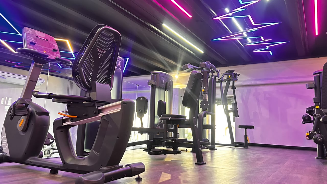 Espaço VIP feminino da Sumrak 408 com bicicleta horizontal, máquinas de força e iluminação em neon nas cores roxo e rosa