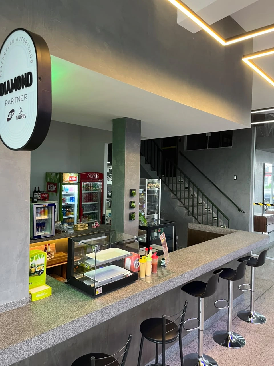 Balcão da cafeteria Sumrak 408 com vitrine, geladeiras de bebidas e bancos