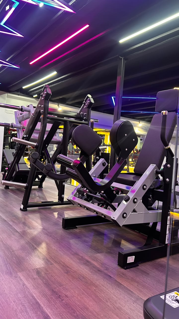 Leg press e máquinas de membros inferiores no espaço VIP feminino da Sumrak 408 com piso de madeira e neon colorido